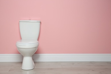 Photo of New ceramic toilet bowl near color wall with space for text