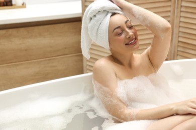 Happy woman taking bath with foam in tub indoors, space for text