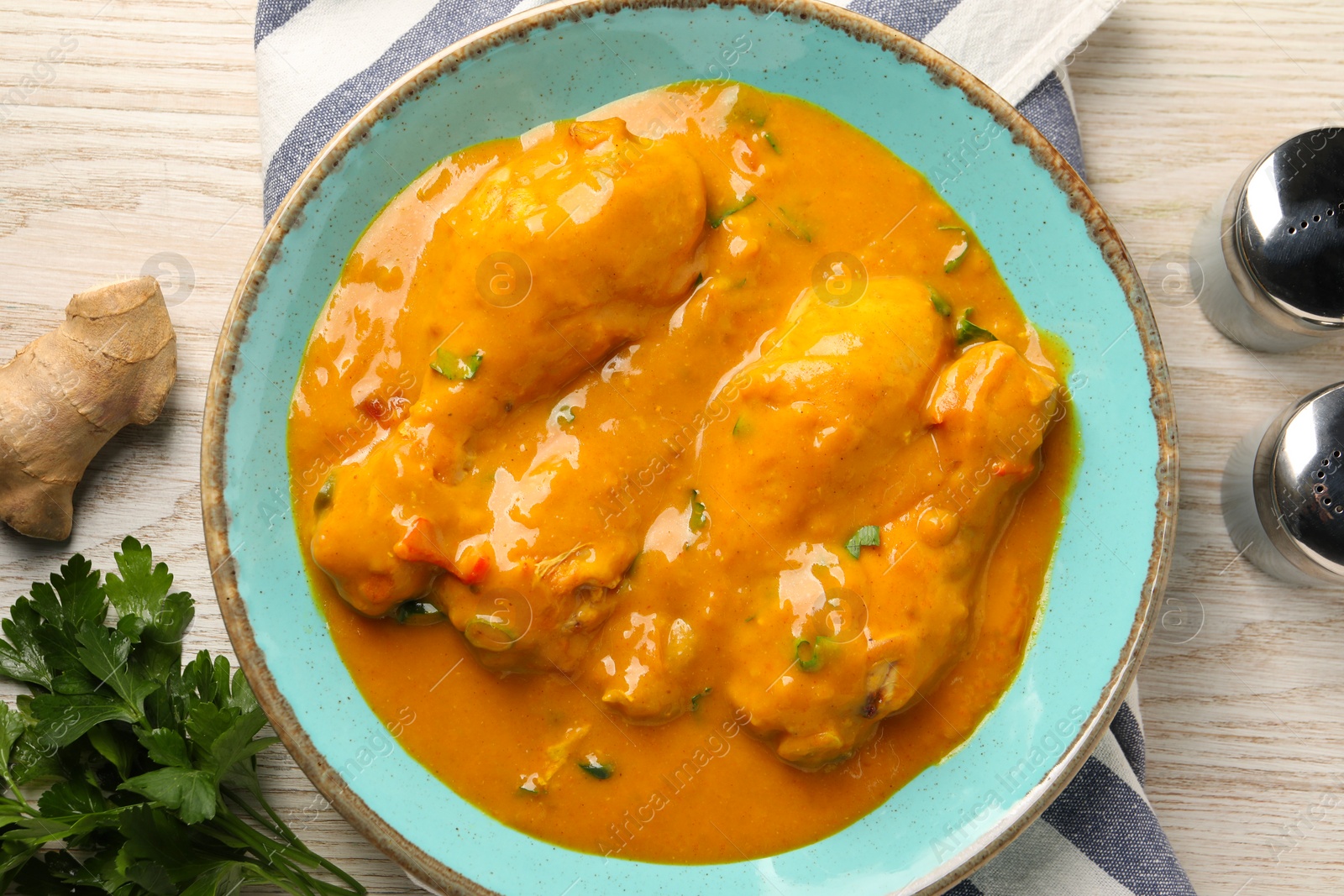 Photo of Tasty chicken curry, parsley and ginger on wooden table, flat lay