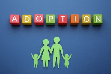 Photo of Family figure and word Adoption made of cubes on blue background, flat lay