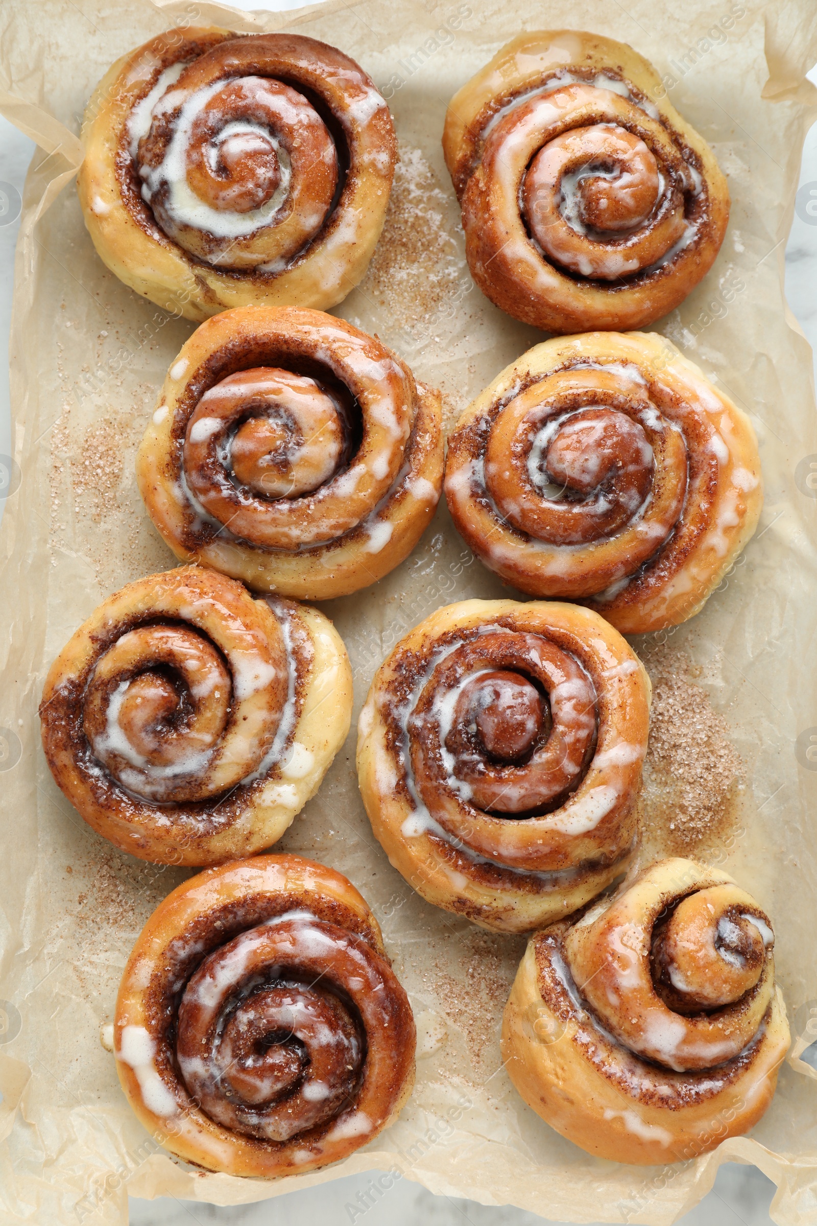 Photo of Tasty cinnamon rolls with cream on parchment, flat lay