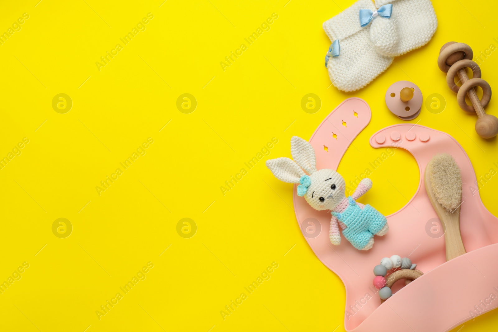 Photo of Flat lay composition with silicone baby bib, toys and accessories on yellow background. Space for text