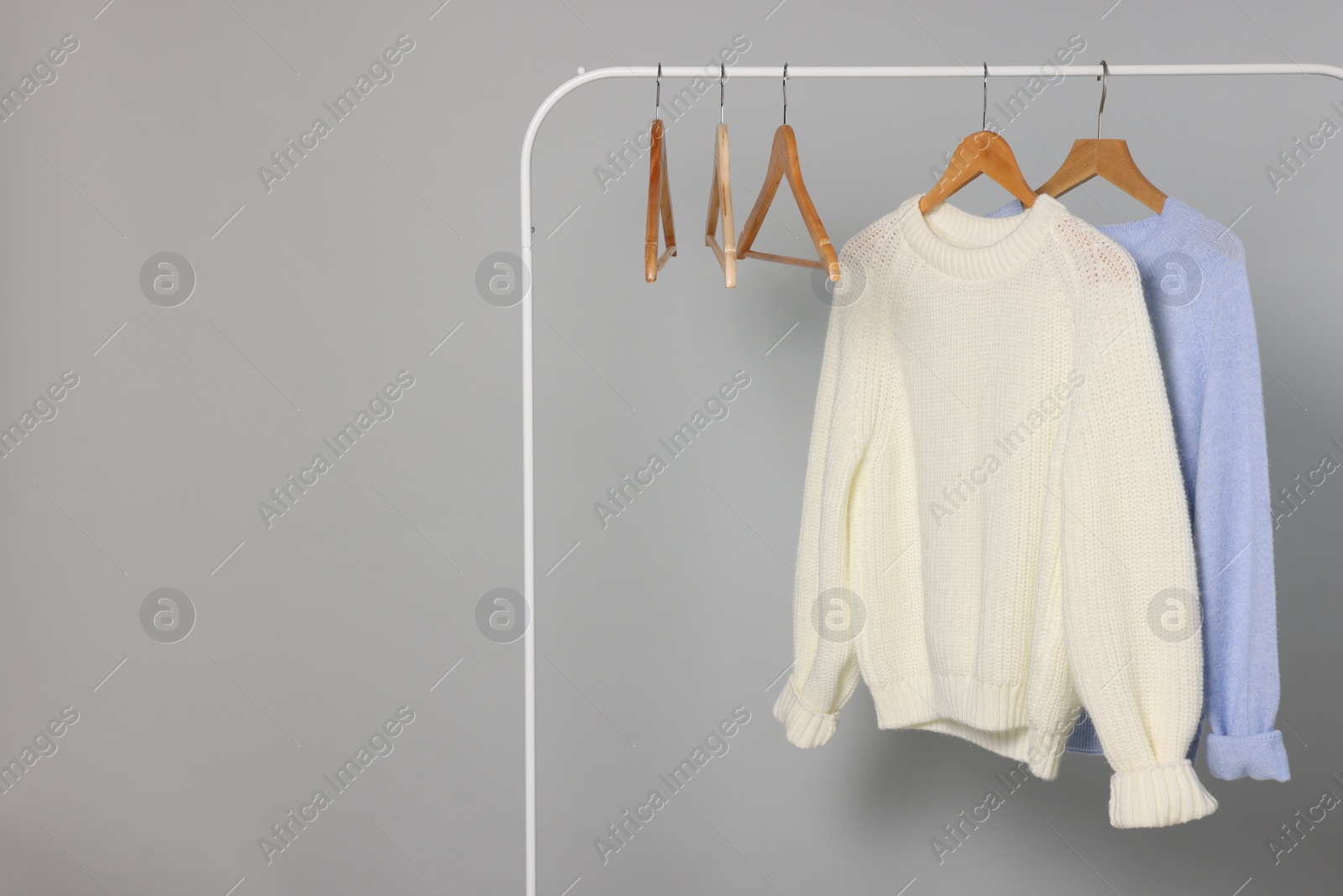 Photo of Rack with warm sweaters and hangers on light grey background. Space for text