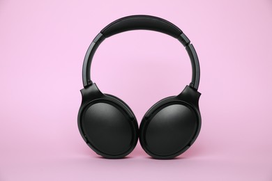 Photo of Modern black wireless headphones on pink background