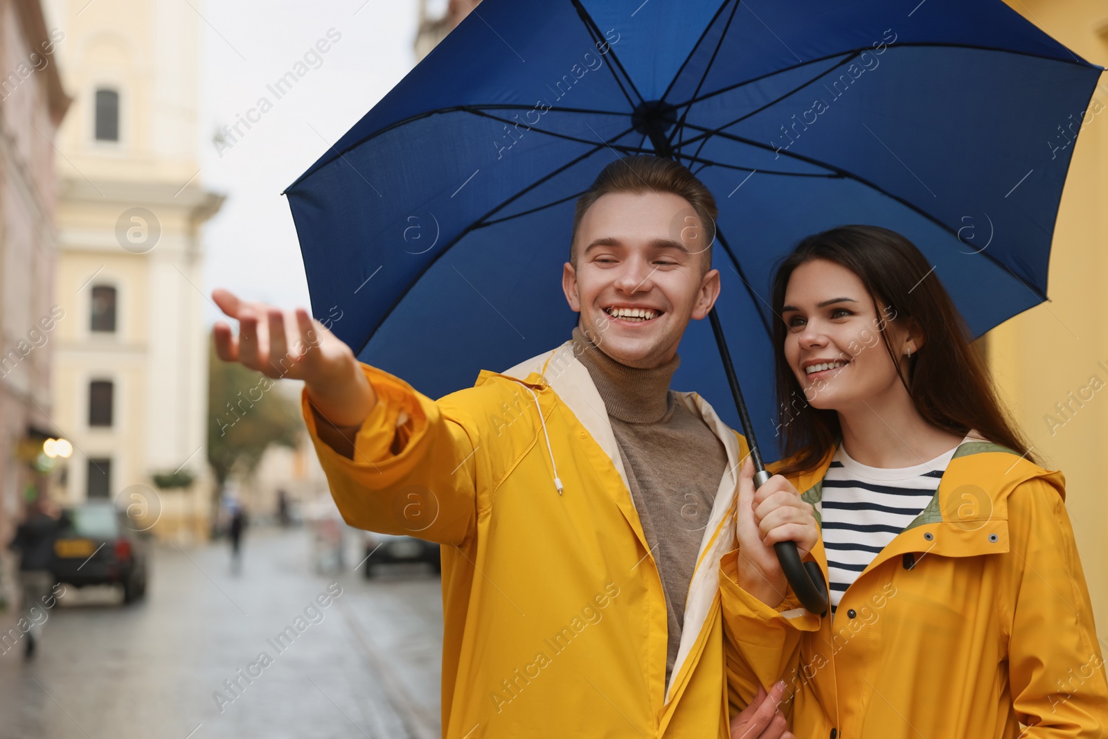 Photo of Lovely young couple with umbrella walking under rain on city street