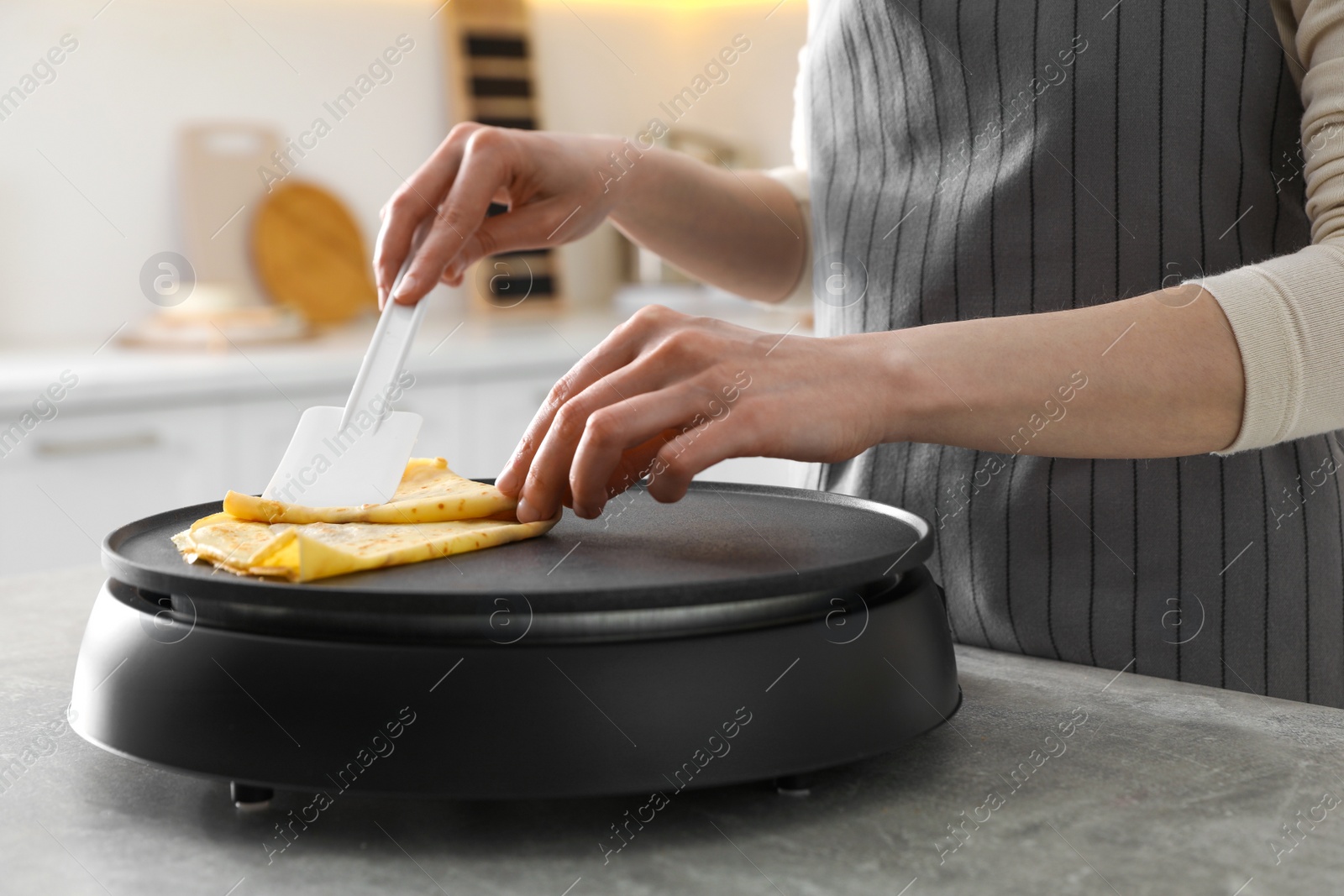 Photo of Woman cooking delicious crepe on electric pancake maker in kitchen, closeup