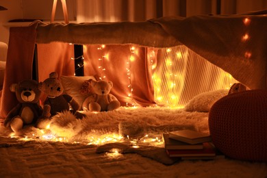 Beautiful play tent decorated with festive lights and toys at home