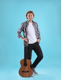 Young man with acoustic guitar on color background