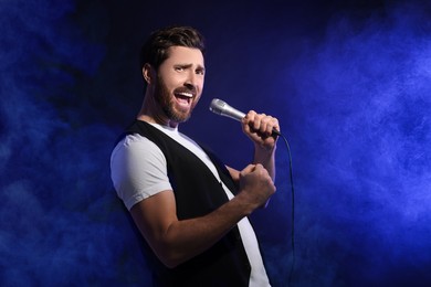 Image of Handsome man with microphone singing on stage in color lighted smoke