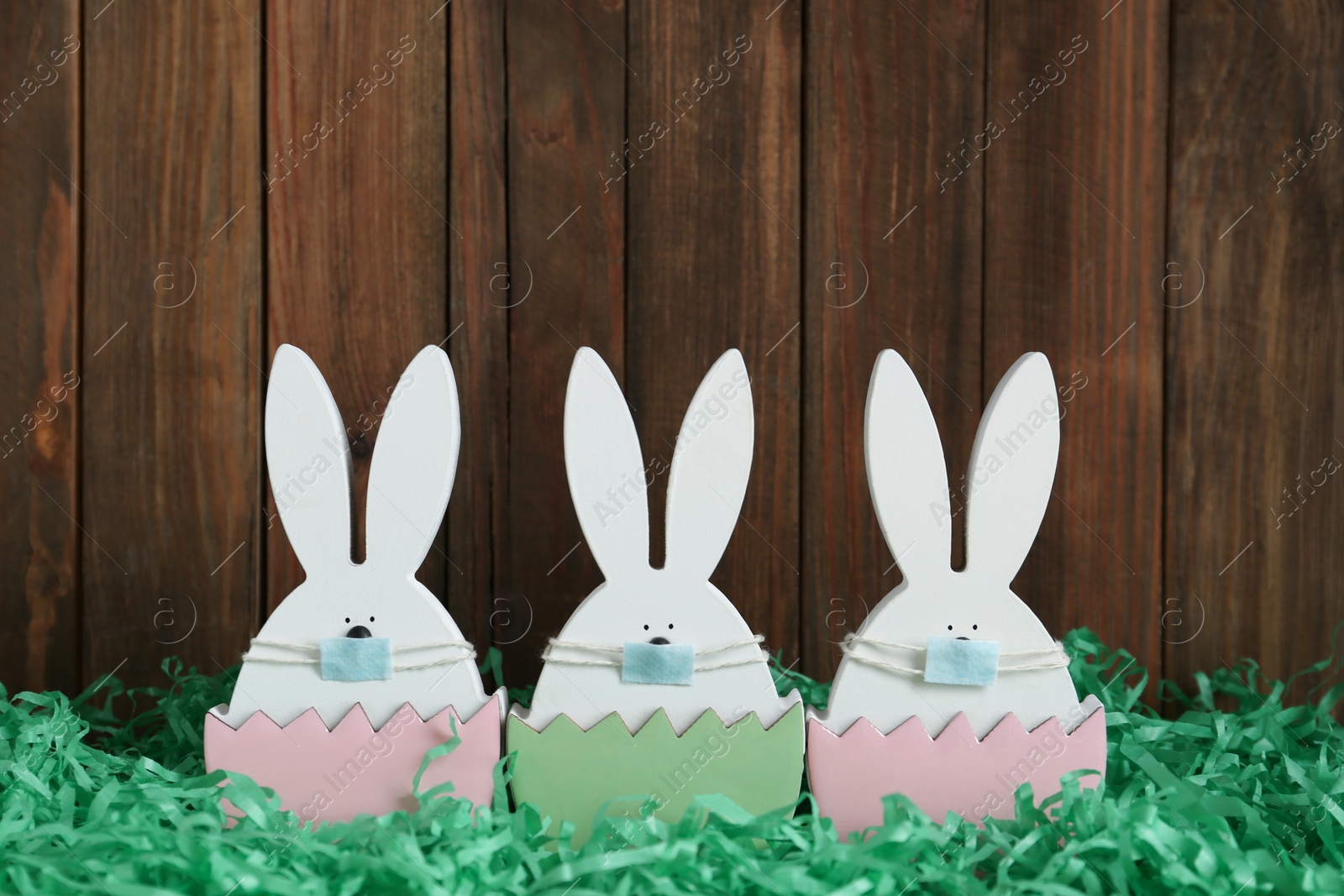 Photo of Cute bunny figures in protective masks on wooden background. Easter holiday during COVID-19 quarantine