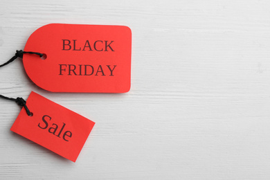 Photo of Red tags with words BLACK FRIDAY SALE on white wooden background, flat lay. Space for text