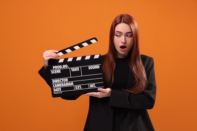 Photo of Shocked actress with clapperboard on orange background. Film industry