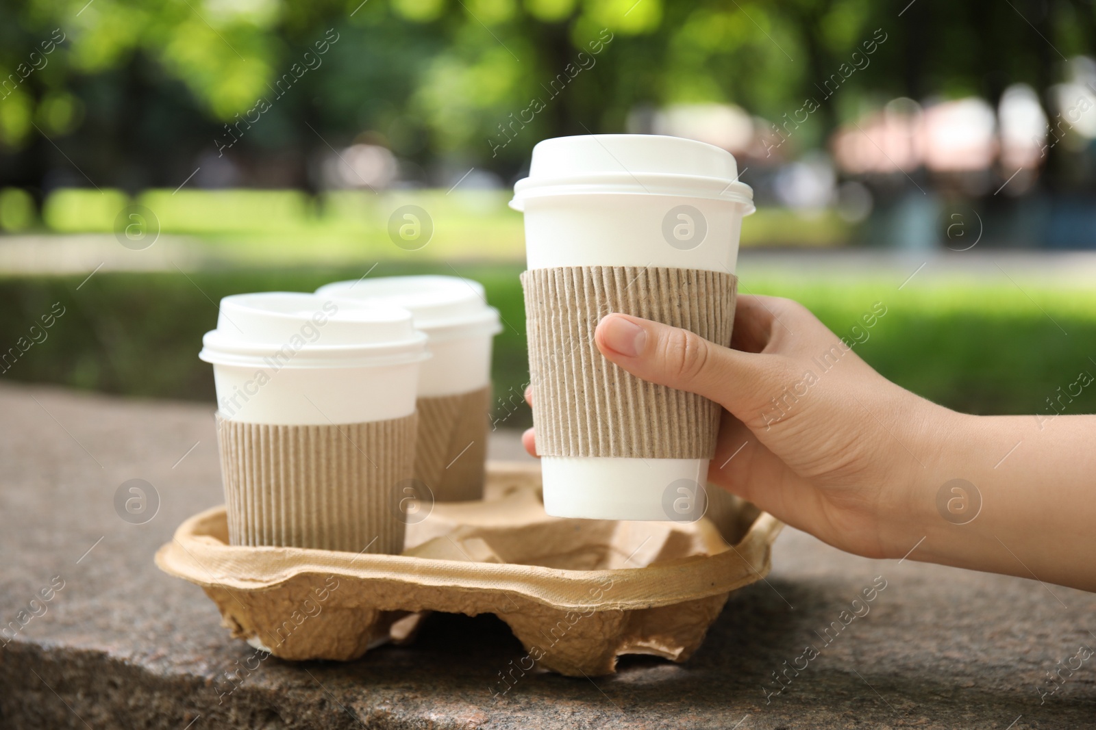 Photo of Woman taking paper coffee cup from cardboard holder outdoors, closeup