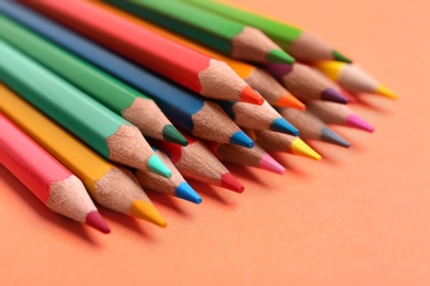 Photo of Different color pencils on coral background, closeup