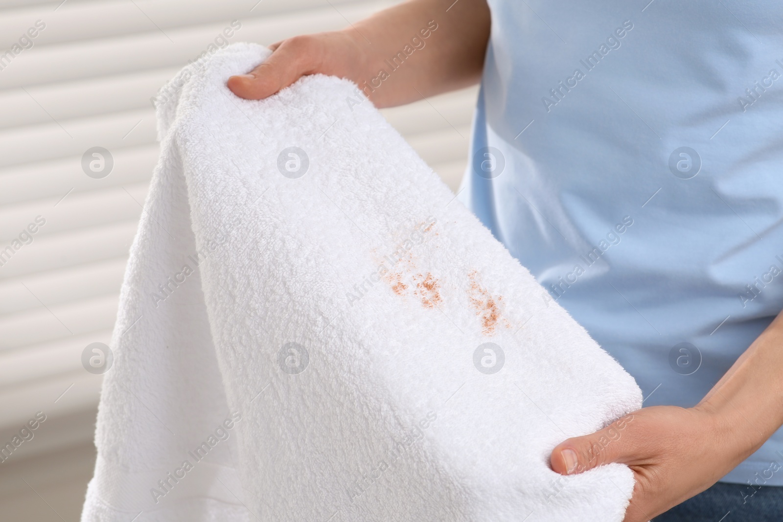 Photo of Woman holding terry towel with makeup spot indoors, closeup