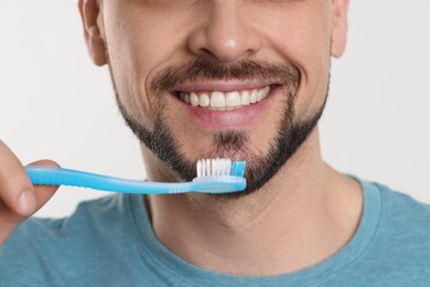 Photo of Man brushing his teeth with plastic toothbrush on white background, closeup