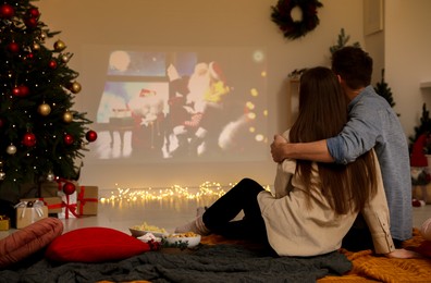 Photo of Couple watching Christmas movie via video projector in cosy room, back view. Winter holidays atmosphere