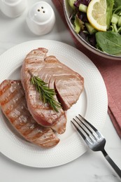 Photo of Delicious tuna steaks with rosemary and salad served on white marble table, flat lay