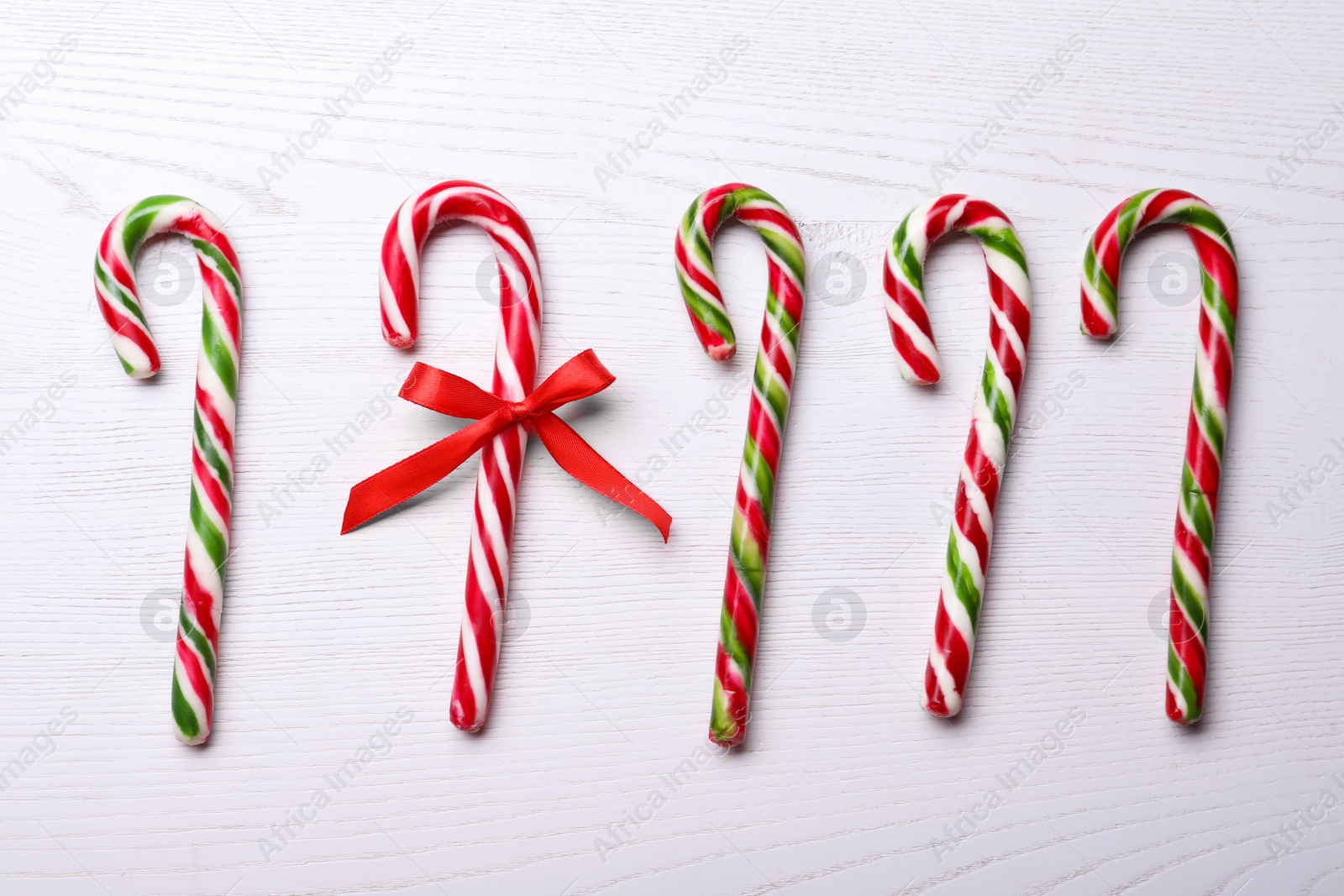 Photo of Sweet Christmas candy canes and one with bow on white wooden table, flat lay