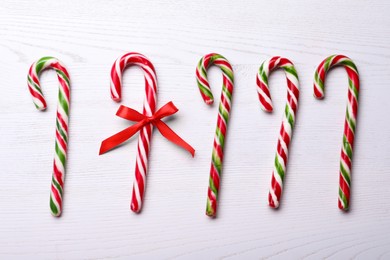 Photo of Sweet Christmas candy canes and one with bow on white wooden table, flat lay