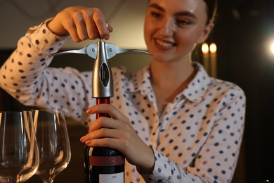 Photo of Romantic dinner. Woman opening wine bottle with corkscrew indoors, selective focus