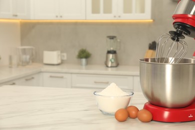 Photo of Modern red stand mixer, eggs and bowl with flour on white marble table in kitchen, space for text