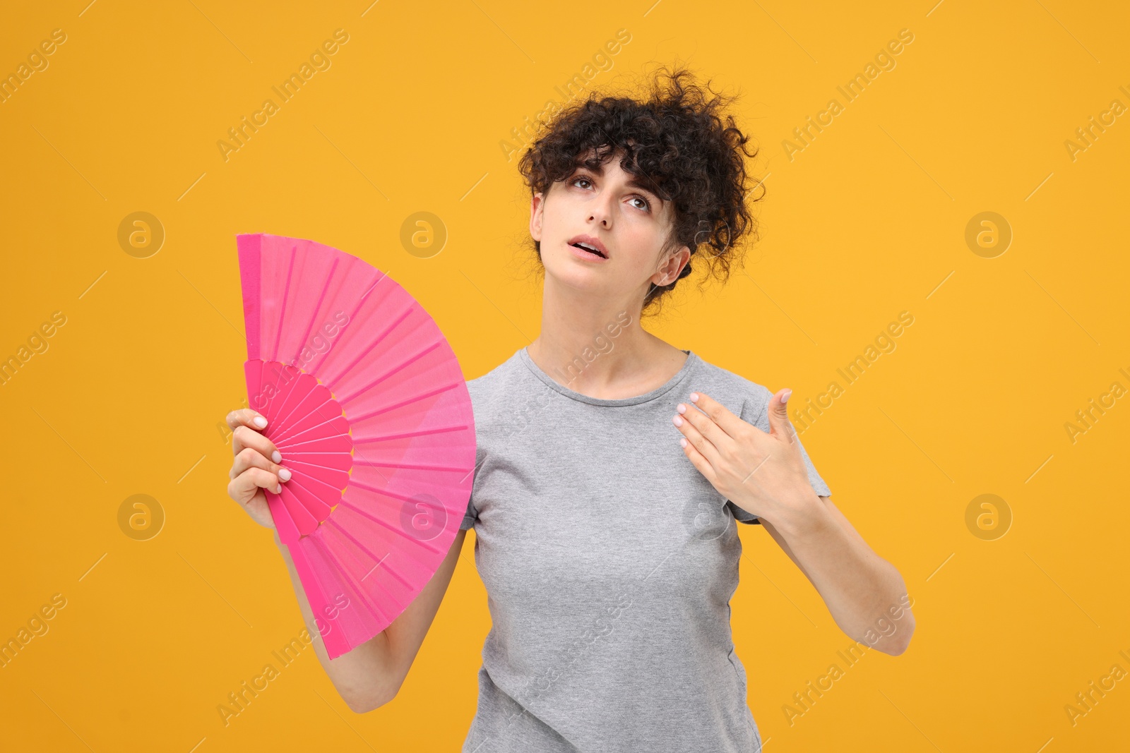 Photo of Woman with hand fan suffering from heat on orange background