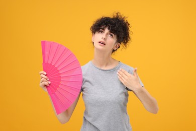 Woman with hand fan suffering from heat on orange background