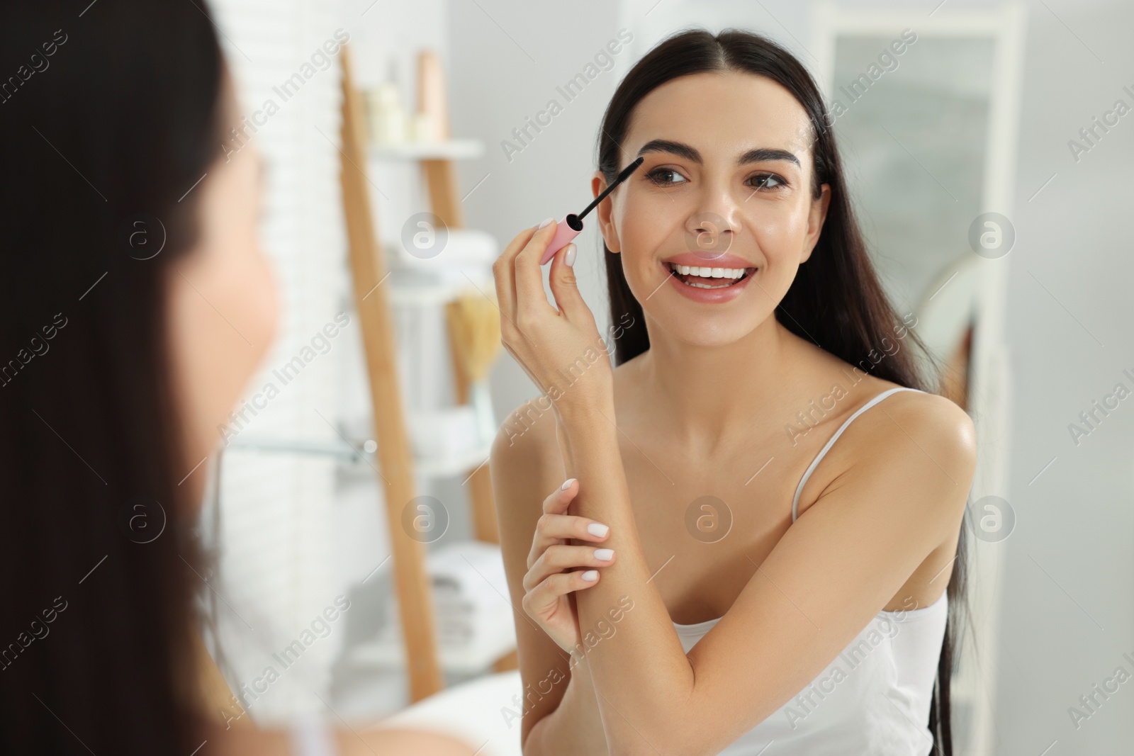 Photo of Beautiful young woman applying mascara near mirror in bathroom