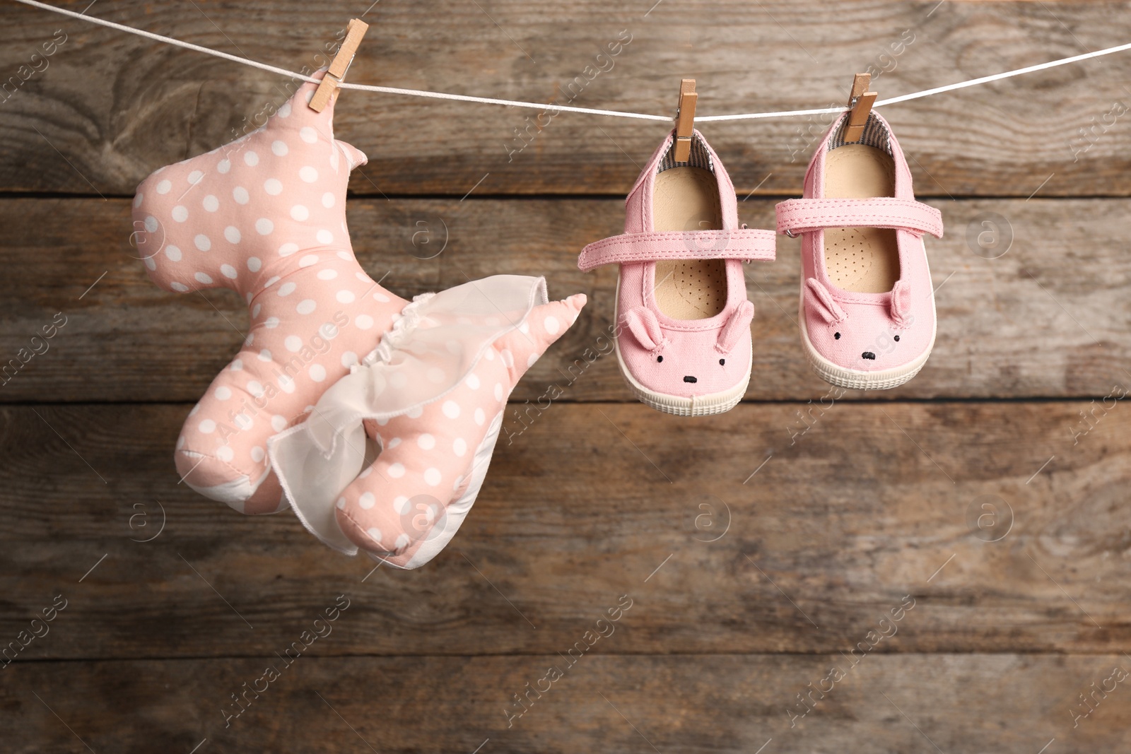 Photo of Toy dog and pair of shoes on laundry line against wooden background. Baby accessories