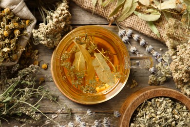 Photo of Freshly brewed tea and dried herbs on wooden table, flat lay