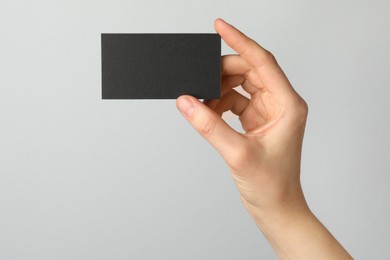 Photo of Woman with blank black business card on light grey background, closeup. Mockup for design