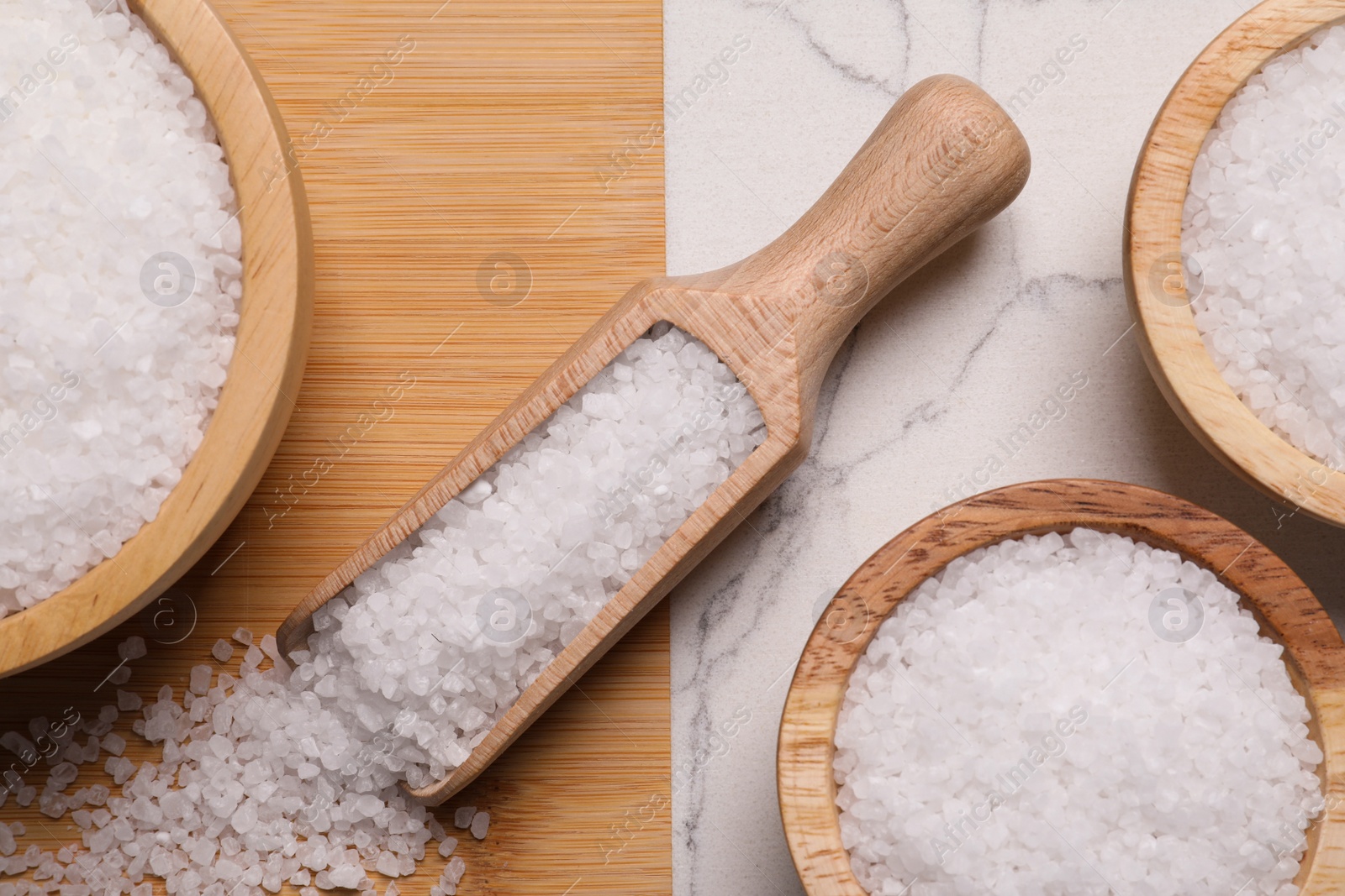 Photo of Wooden board with natural sea salt in scoop and bowls on white marble table, flat lay