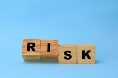 Photo of Wooden cubes with word Risk on light blue background