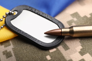 Photo of Military ID tag, bullet and Ukrainian flag on pixel camouflage, closeup