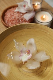 Bowl with water, flowers, sea salt and burning candles on bamboo mat, closeup. Spa treatment