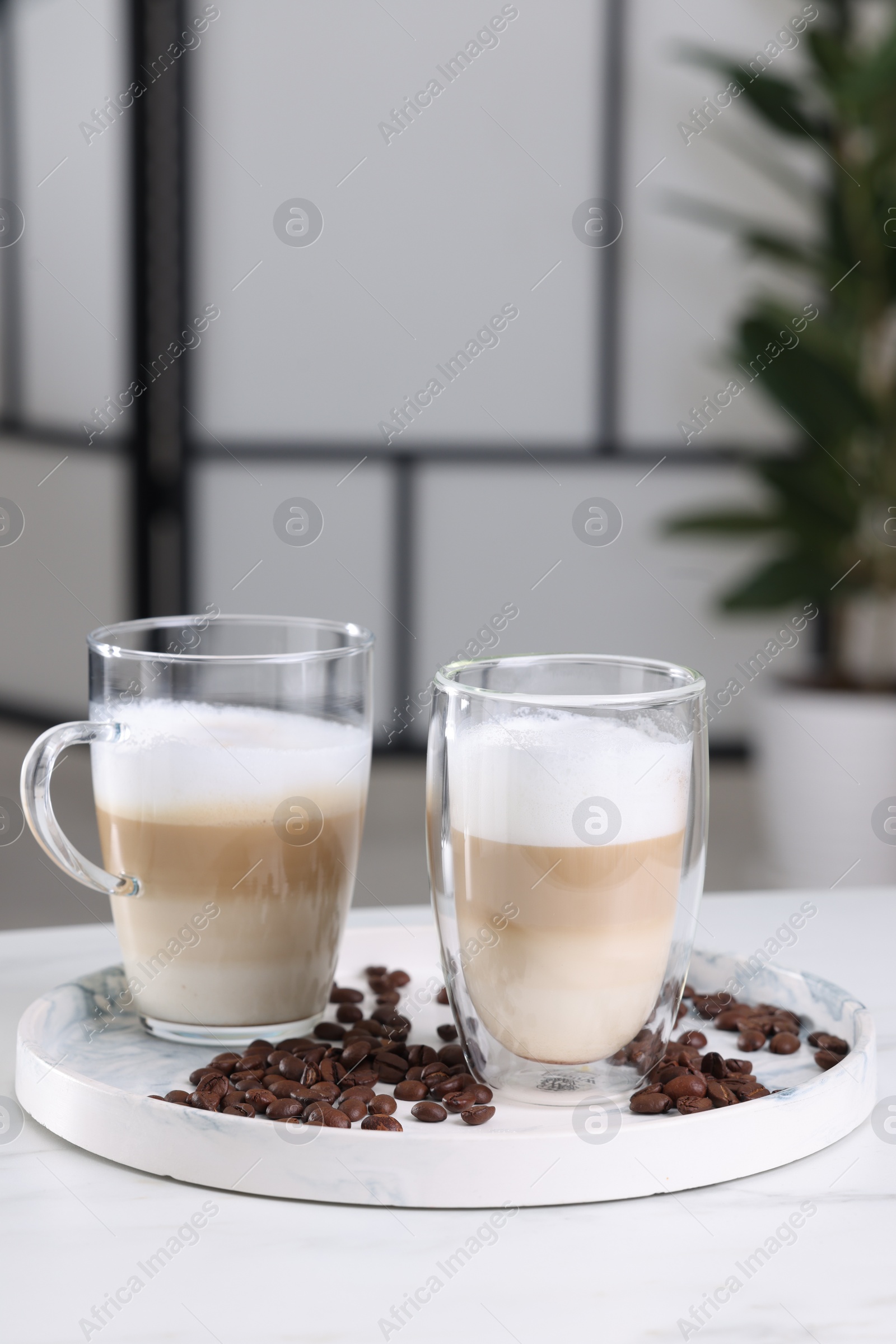 Photo of Aromatic latte macchiato and coffee beans on white marble table against blurred background