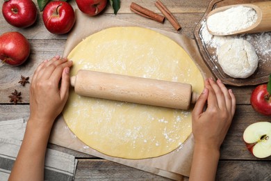 Photo of Woman rolling dough for apple pie at wooden table, top view