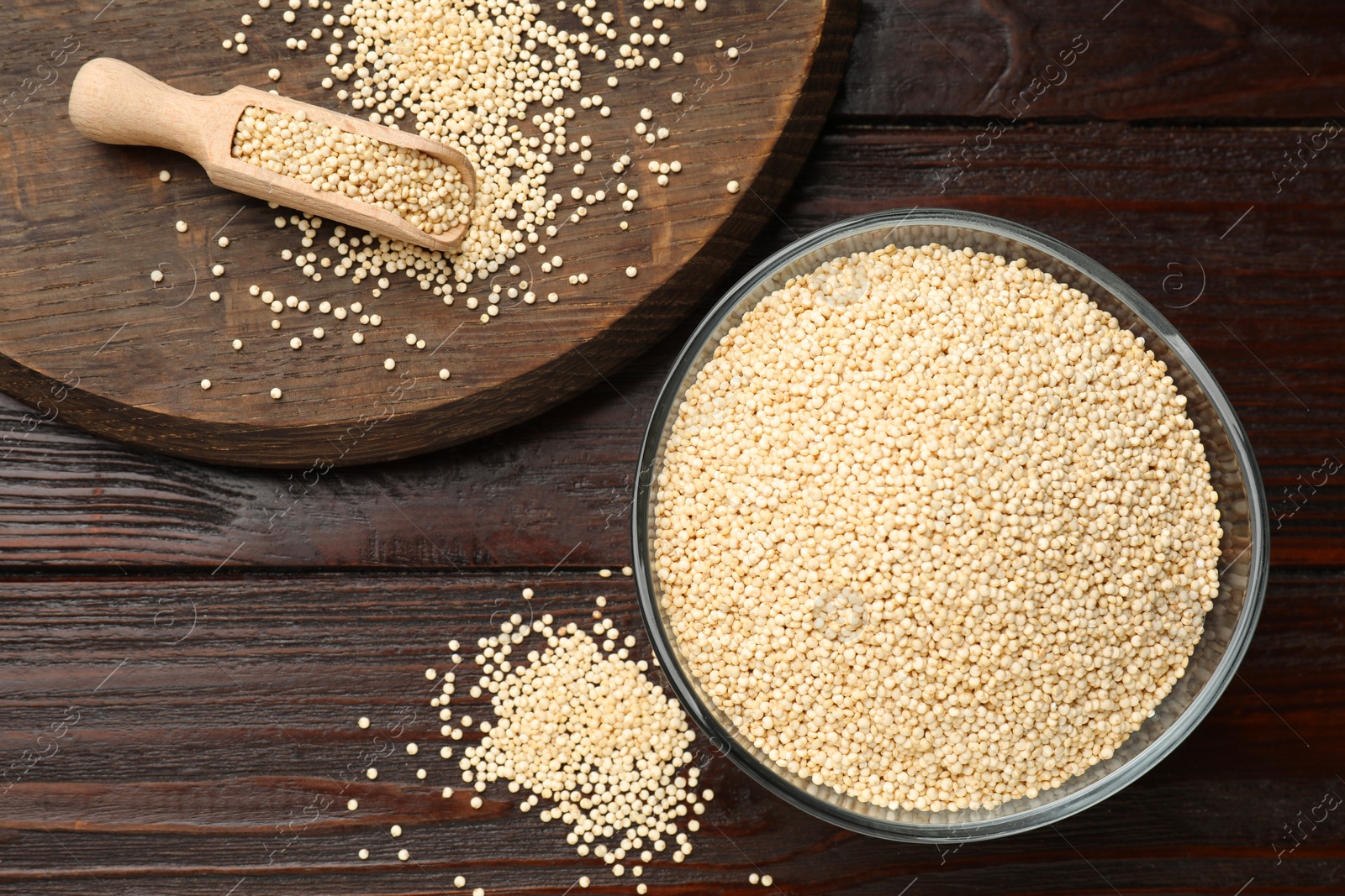 Photo of Dry quinoa seeds in bowl and scoop on wooden table, flat lay