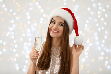 Photo of Happy young woman in Santa hat with champagne against blurred Christmas lights