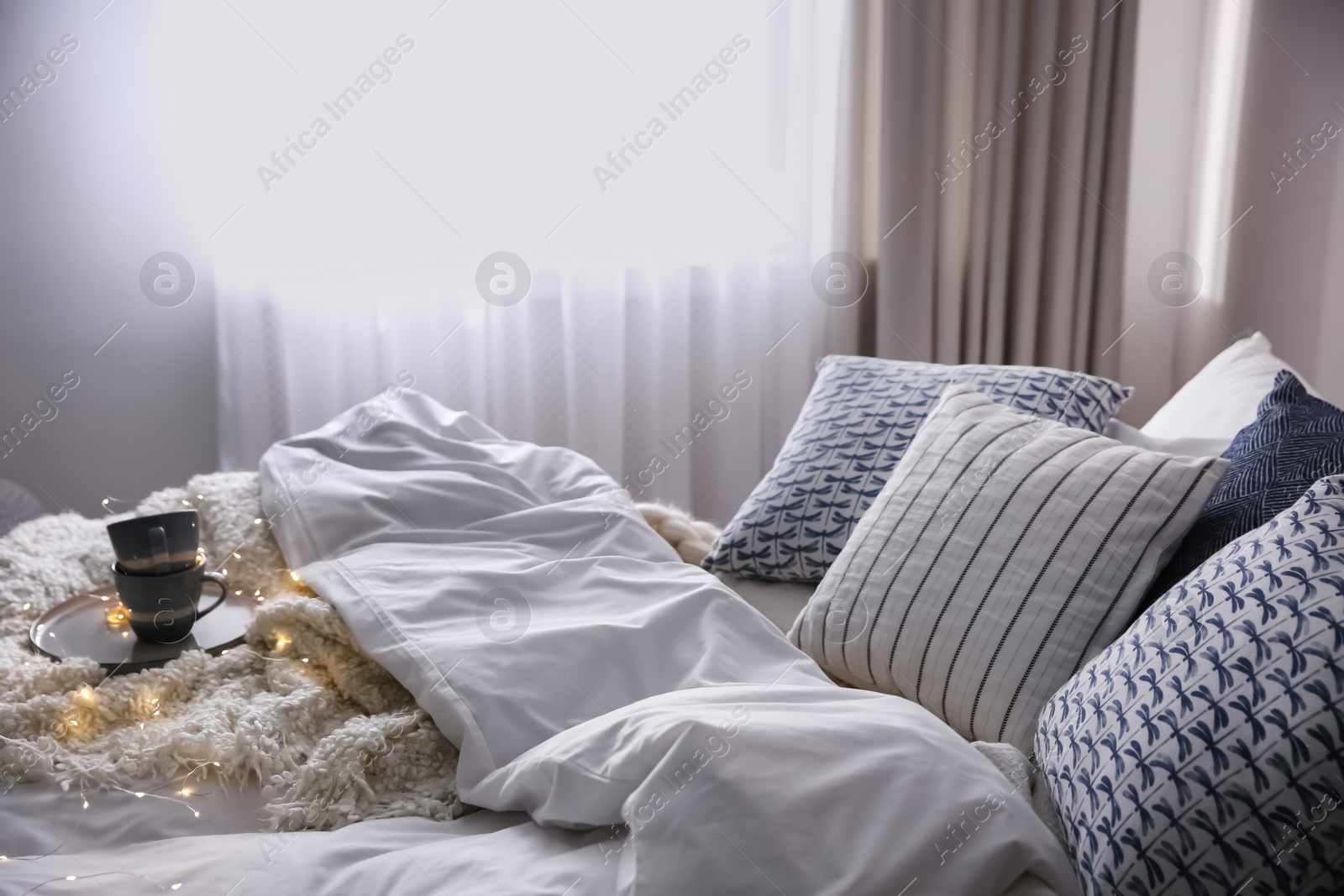 Photo of Bed with warm blanket and cushions in room. Interior design