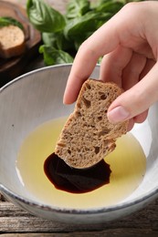 Photo of Woman dipping piece of bread into balsamic vinegar with oil at wooden table, closeup