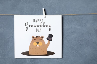 Photo of Happy Groundhog Day greeting card hanging against blue background, space for text