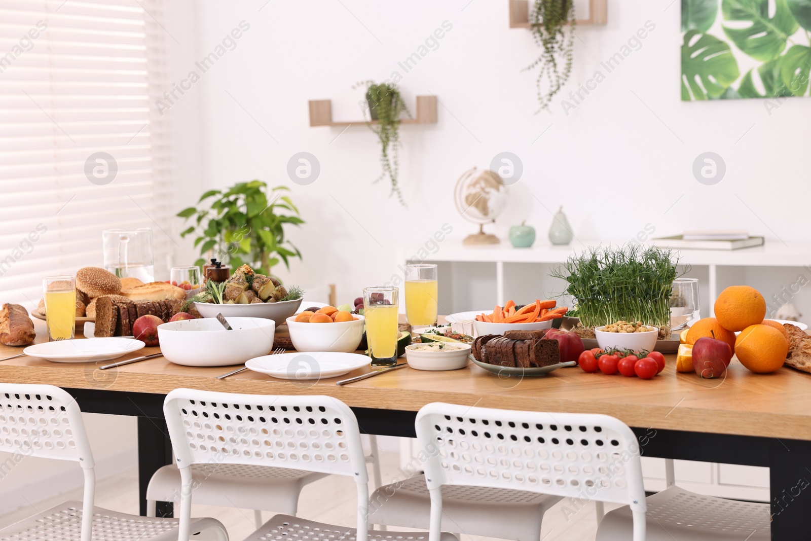 Photo of Healthy vegetarian food, glasses of juice, cutlery and plates on wooden table indoors