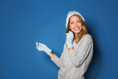 Happy young woman wearing warm sweater, knitted hat and mittens on blue background