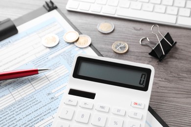 Tax accounting. Calculator, document, stationery and coins on wooden table, closeup