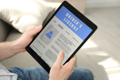 Photo of Man holding tablet with driver's license application form at home, closeup