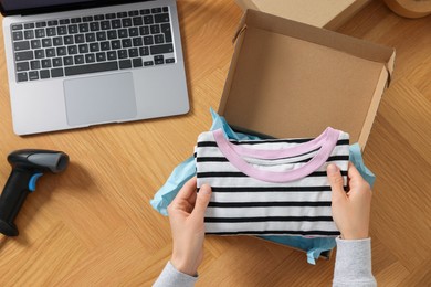Photo of Woman packing clothes into cardboard box at wooden table, top view. Online store