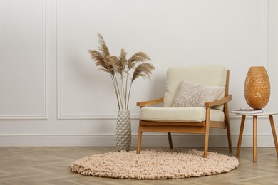 Photo of Stylish armchair with cushion, spikes and lamp near white wall indoors, space for text. Interior design