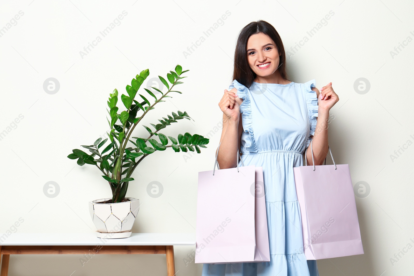 Photo of Beautiful young woman with blank paper bags near white wall, space for text